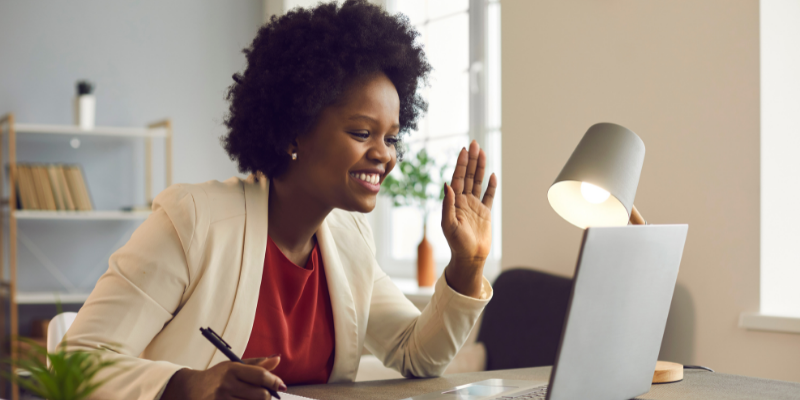 Young person working remotely. Sitting at home on their latop. Waving at their screen. 